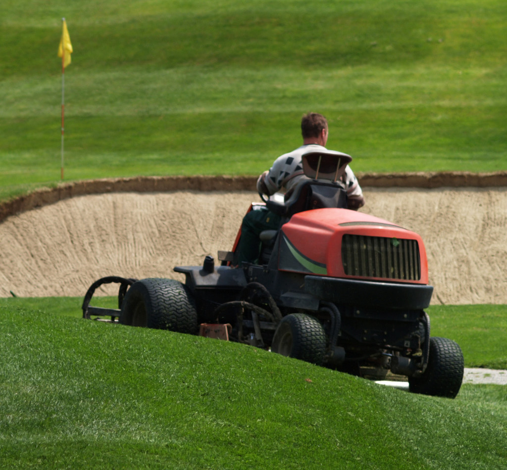 Greenkeeper. Golf course maintenance worker, cutting green grass.